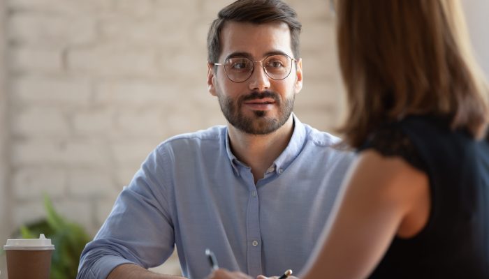 Head shot pleasant young businessman in eyeglasses holding meeting with female partner. Happy male entrepreneur listening to colleague. Friendly smiling teammates discussing project ideas at office.